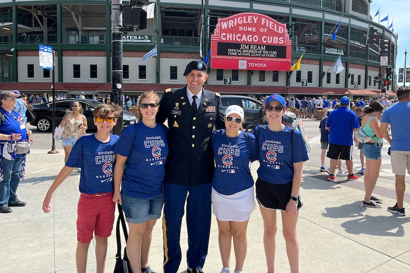 U.S. Army Reserve Lt. Col. Benjamin Dykstra, center, stands in front of the Chicago Cubs marquee, with his family, at Wrigley Field in Chicago, May 30, 2022, before a military game recognition.