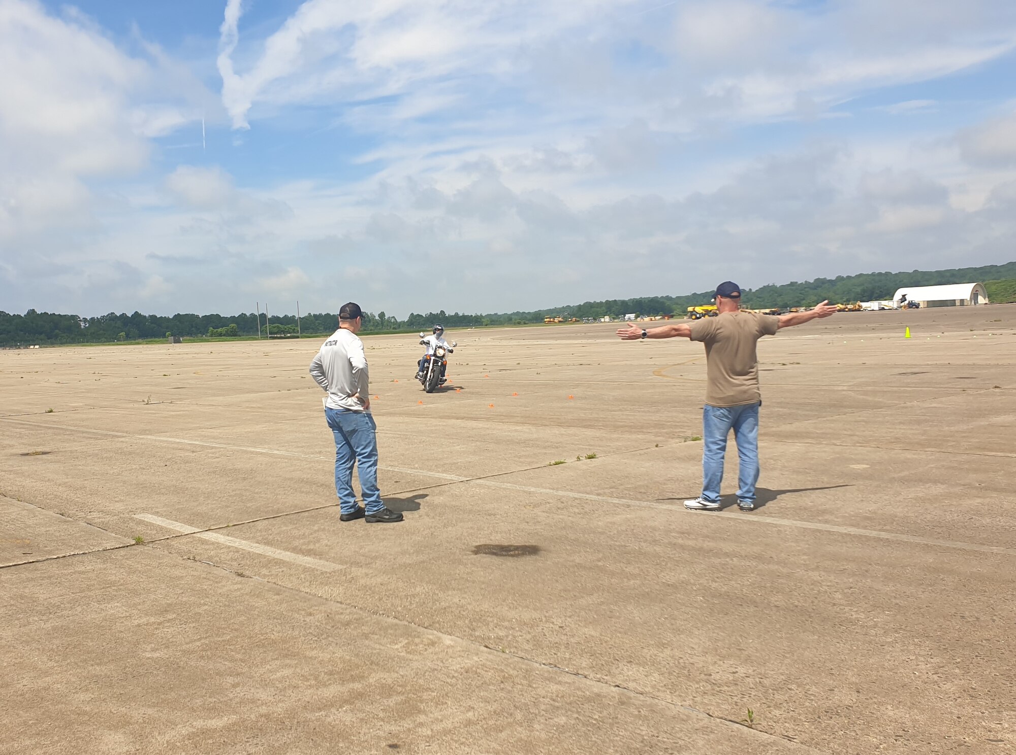 Two men facing a man riding a motorcycle on an airfield.