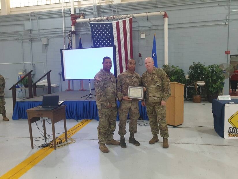 Three uniformed military men stand together holding an award certificate.