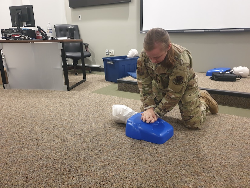 Female in military uniform practices CPR on a dummy.