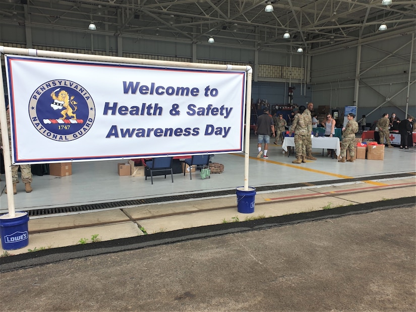 Health and Safety Day sign with displays and uniformed military members to the right of the sign.
