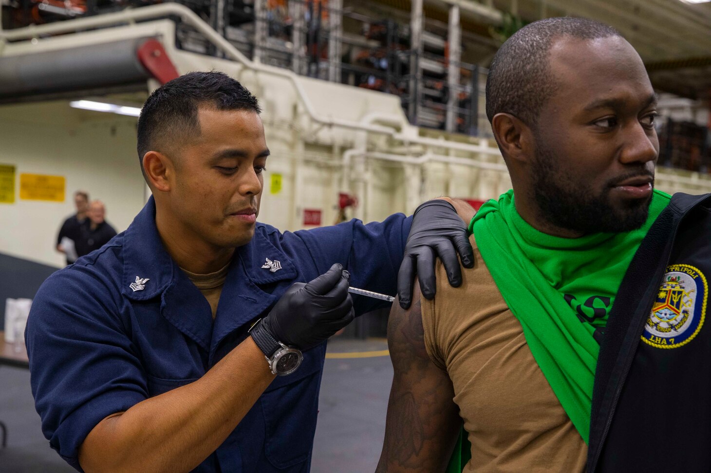 Hospital Corpsman 1st Class Christopher McCloskey, from Oceanside, California, left, gives a typhoid vaccine to a Sailor in the hangar bay aboard amphibious assault carrier USS Tripoli (LHA 7), May 17, 2022. Tripoli is underway conducting routine operations in U.S. 7th Fleet. (U.S. Navy photo by Mass Communication Specialist 3rd Class Maci Sternod)