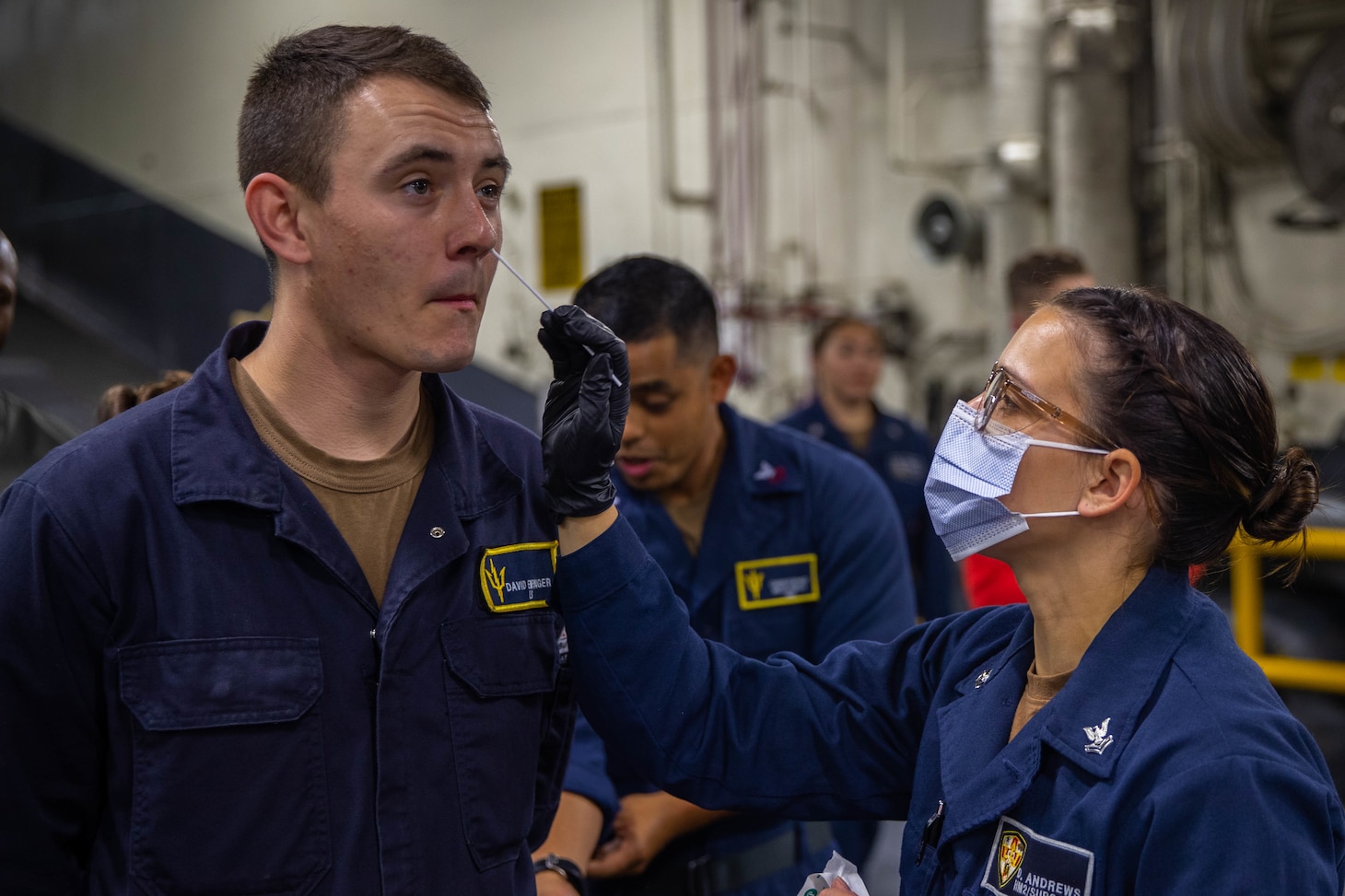 Hospital Corpsman 2nd Class Darian Andrews, from Defiance, Ohio, right, administers a COVID-19 test in the vehicle stowage area aboard amphibious assault carrier USS Tripoli (LHA 7), May 19, 2022. Tripoli is underway conducting routine operations in U.S. 7th Fleet. (U.S. Navy photo by Mass Communication Specialist 3rd Class Maci Sternod)