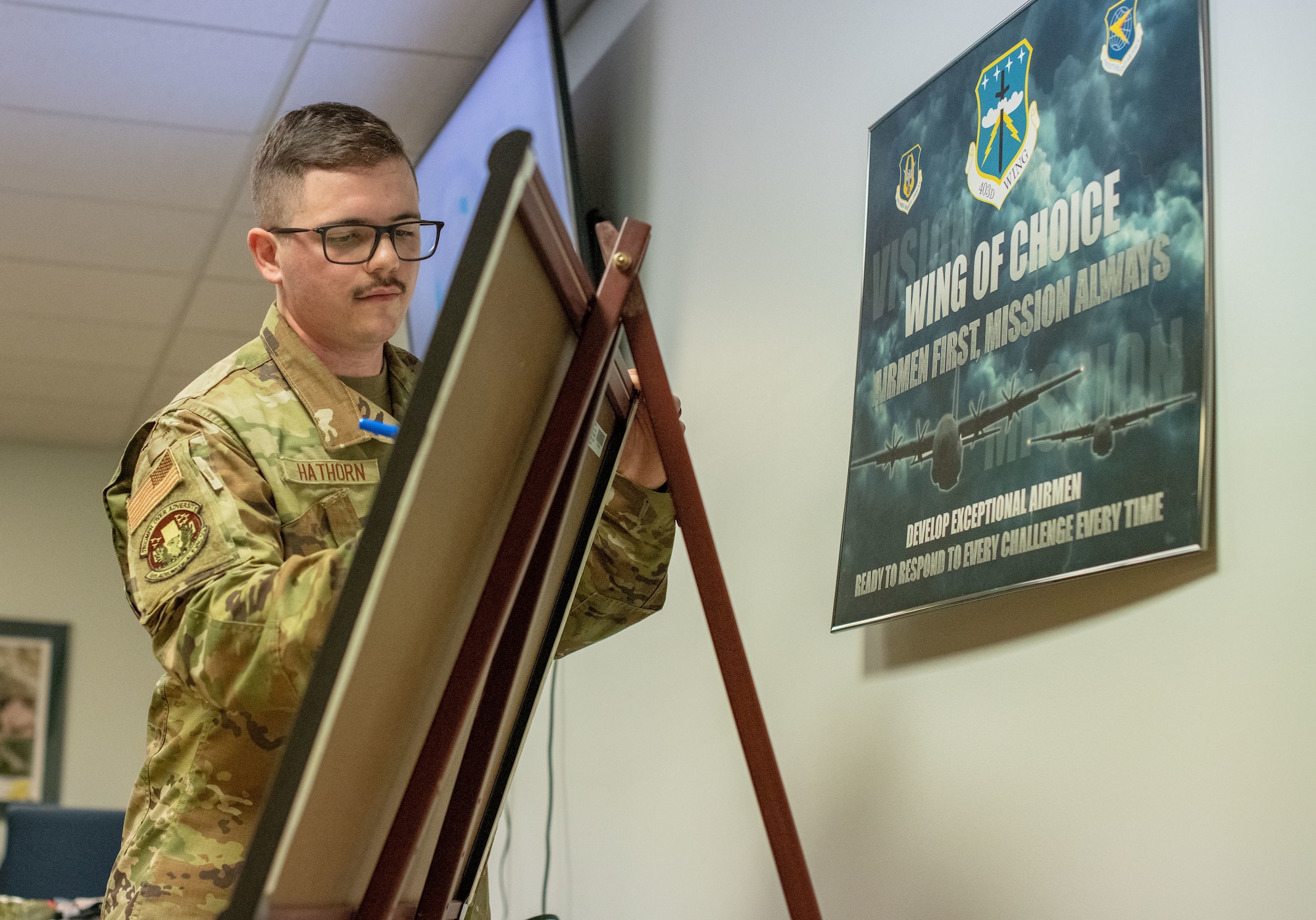 An Airmen writes on a whiteboard that is sitting on a three-legged stand