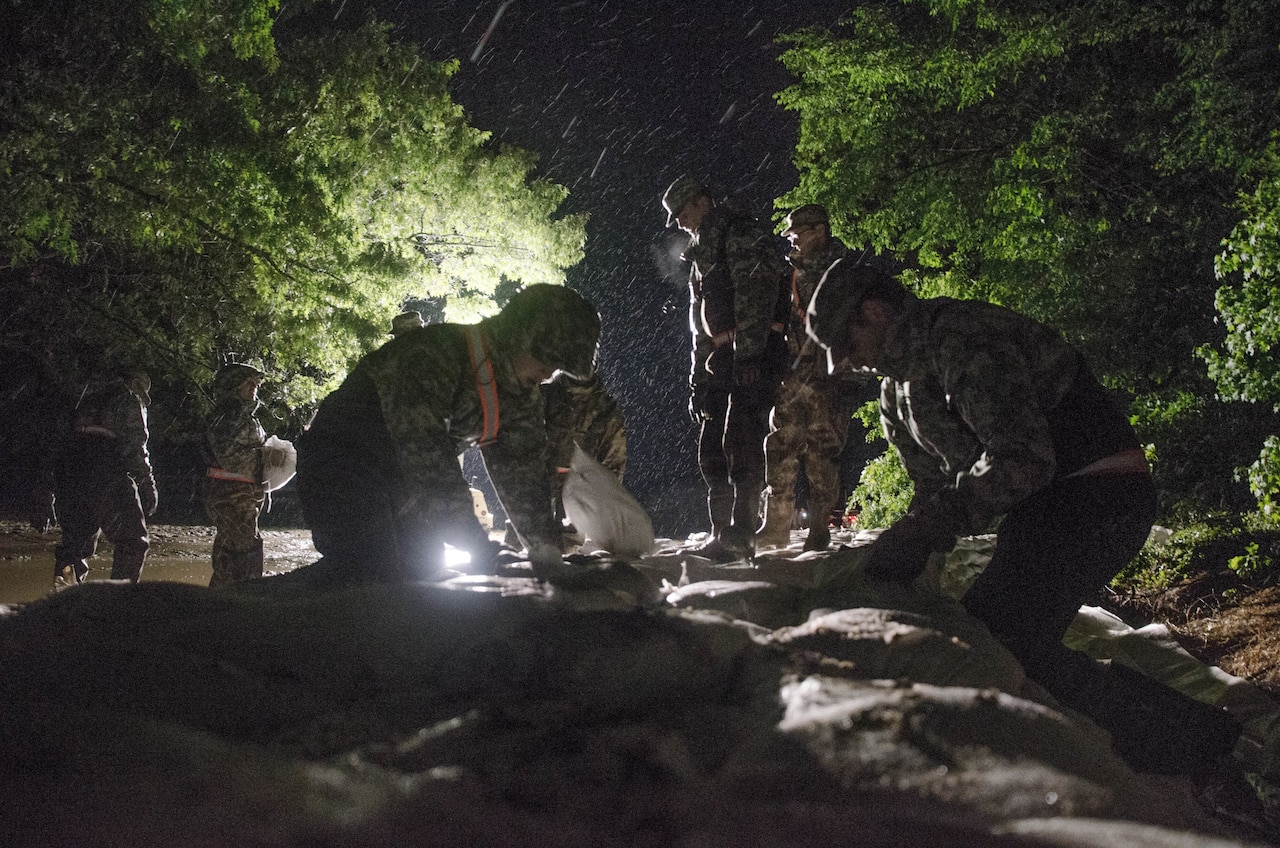 Service members put sandbags into place in the dark.