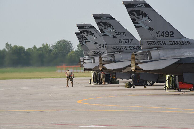 Military fighter aircraft sit near each other. A service member stands near one of the aircraft.
