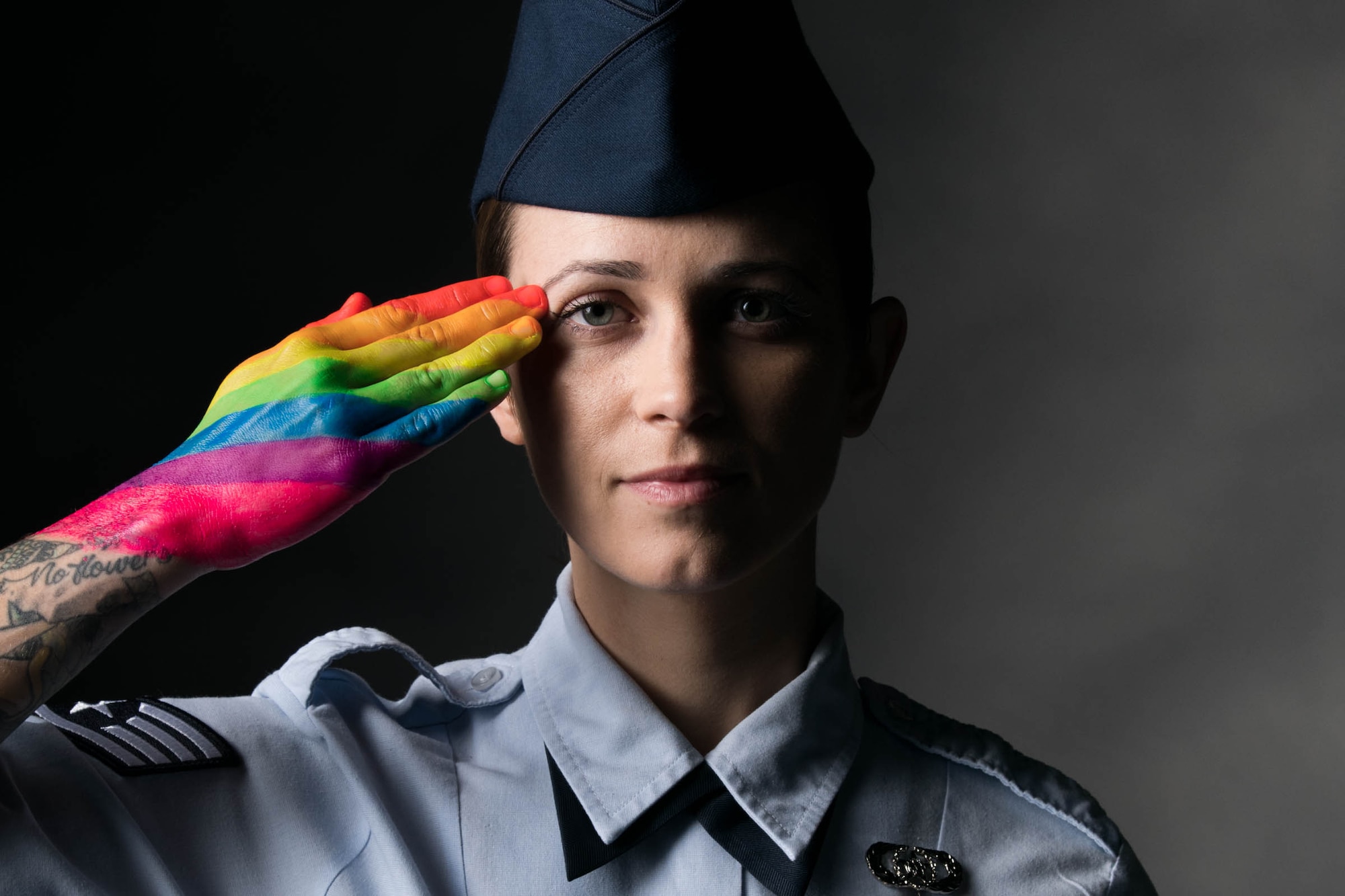 A service member poses for a portrait and salutes with a rainbow-painted hand.