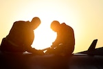 Two service members sit atop an aircraft.