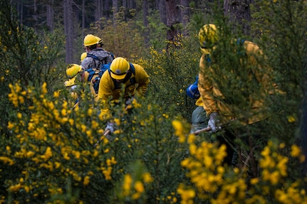 Guardsmen wearing protective gear use hand tools in a field during training.