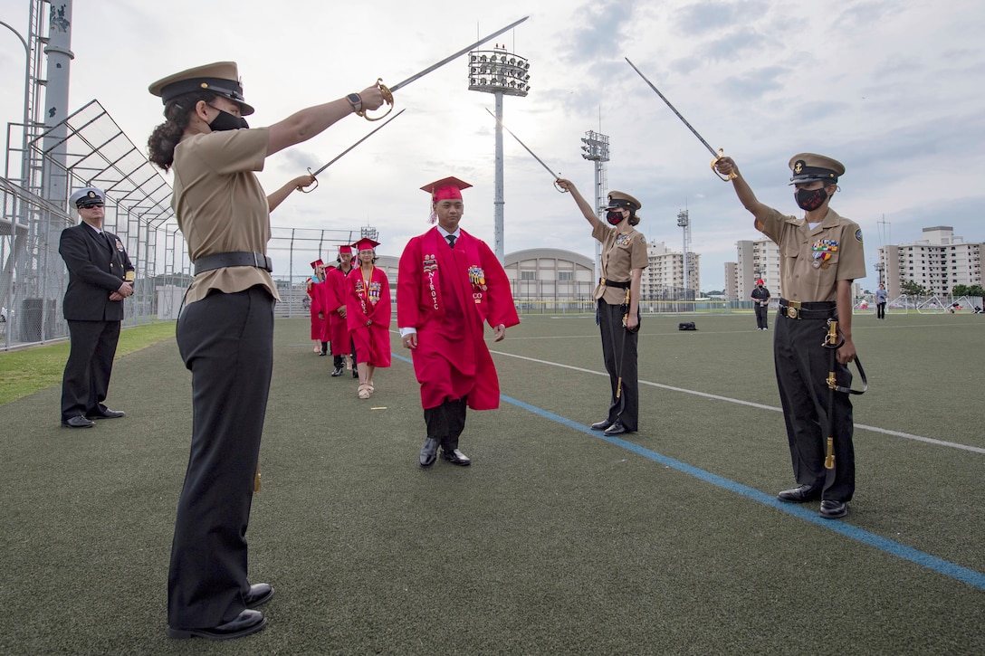 Sailors hold swords in the air as people in graduation gowns walk beneath them.