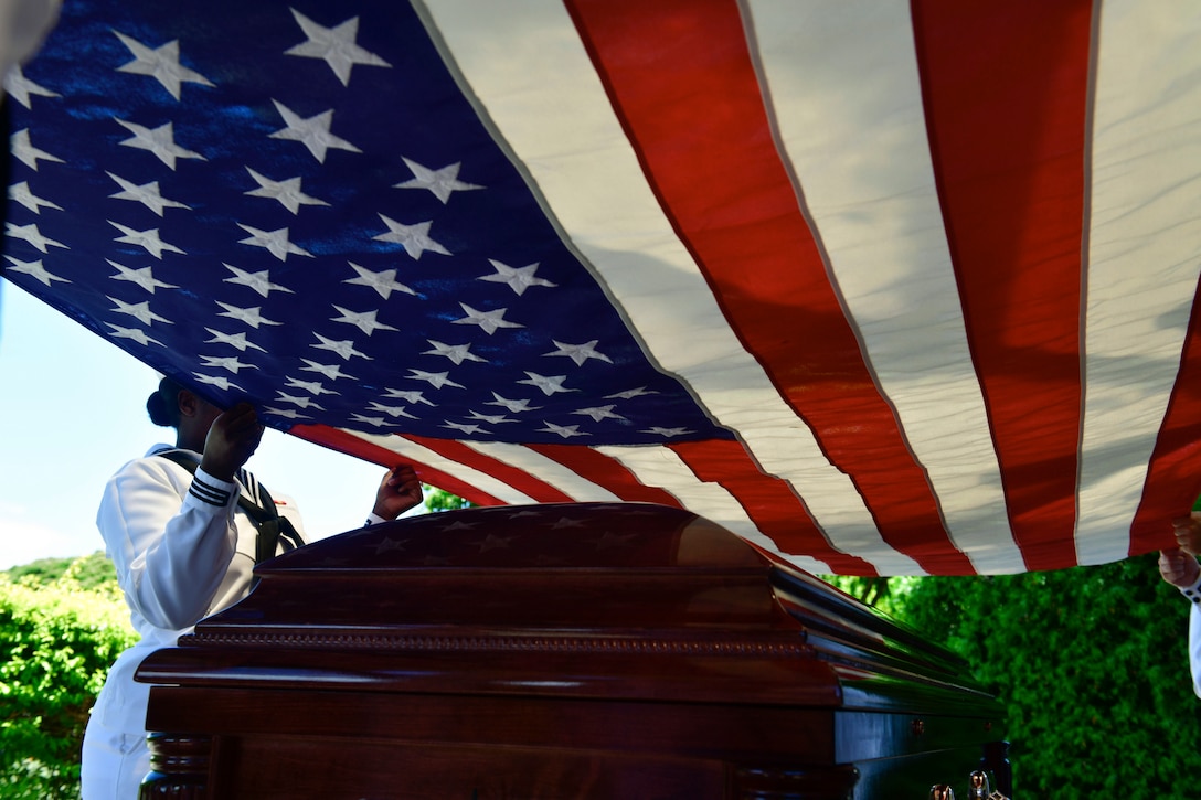 Sailors hold an American flag over a casket during a ceremony.