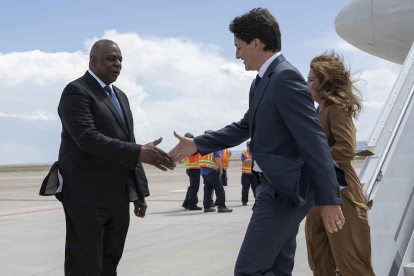 A man in a business suit wearing shakes hands with another man in a business suit while his wife looks on.