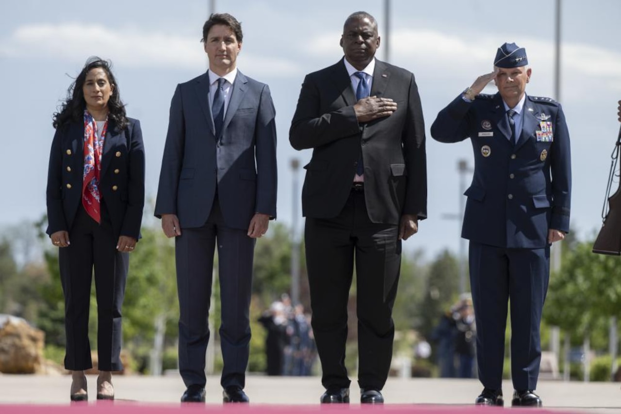 Three people and one service member stand shoulder to shoulder while paying respect to their national anthem.