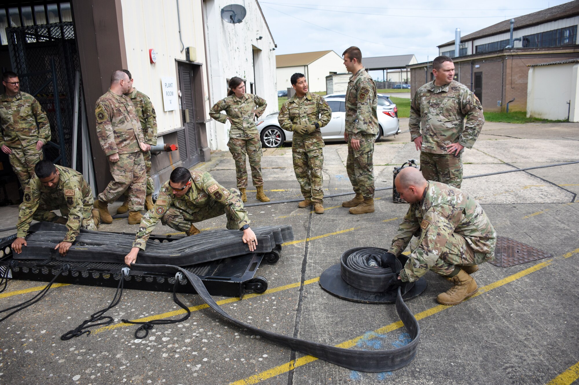 Three men pack a 4-inch fuel hose on a sled while seven other people watch.