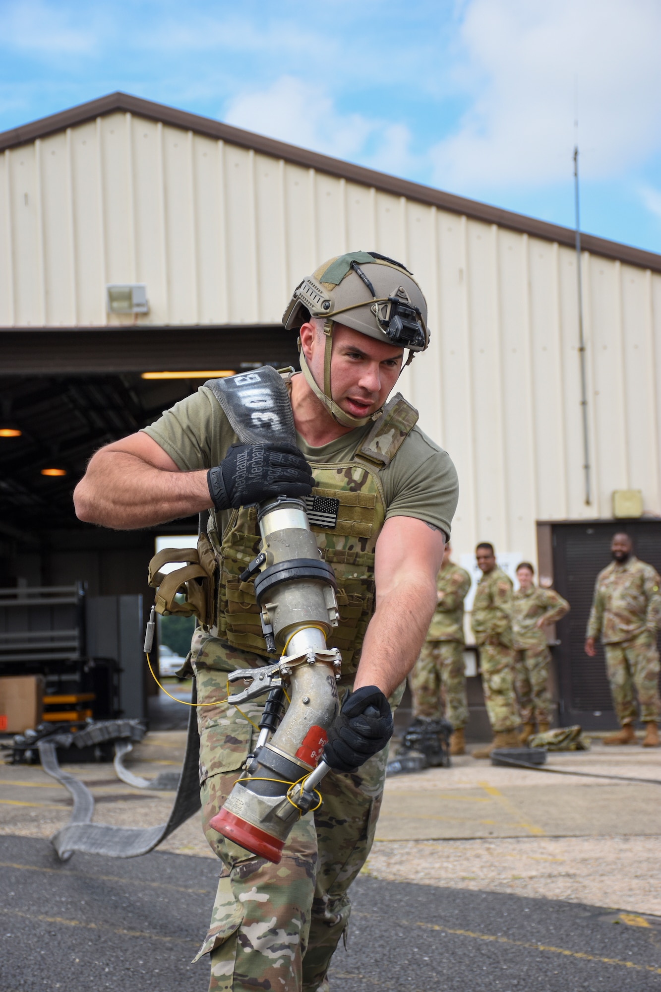 A man in body armor and a ballistic helmet pulls a 4-inch fuel hose over his shoulder.