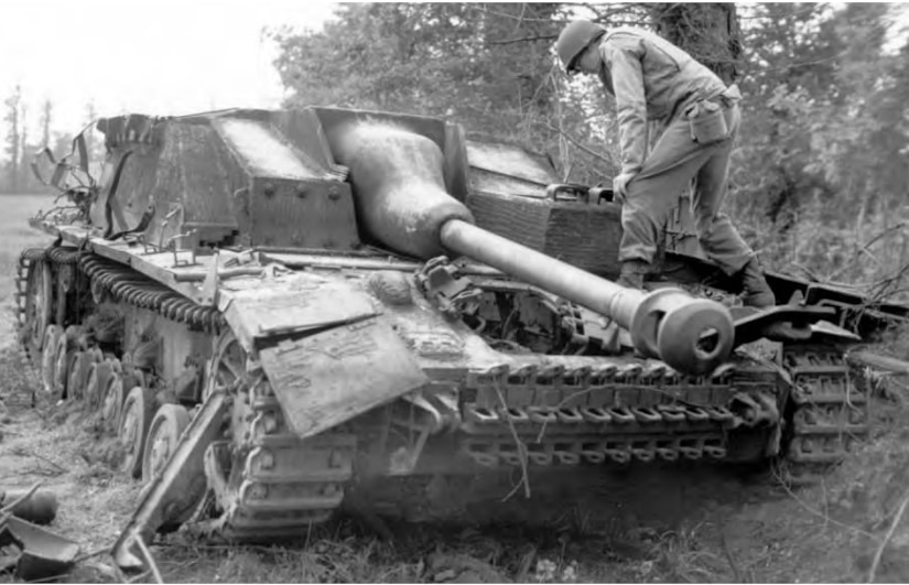 A man stands on the front of a damaged tank to examine it.