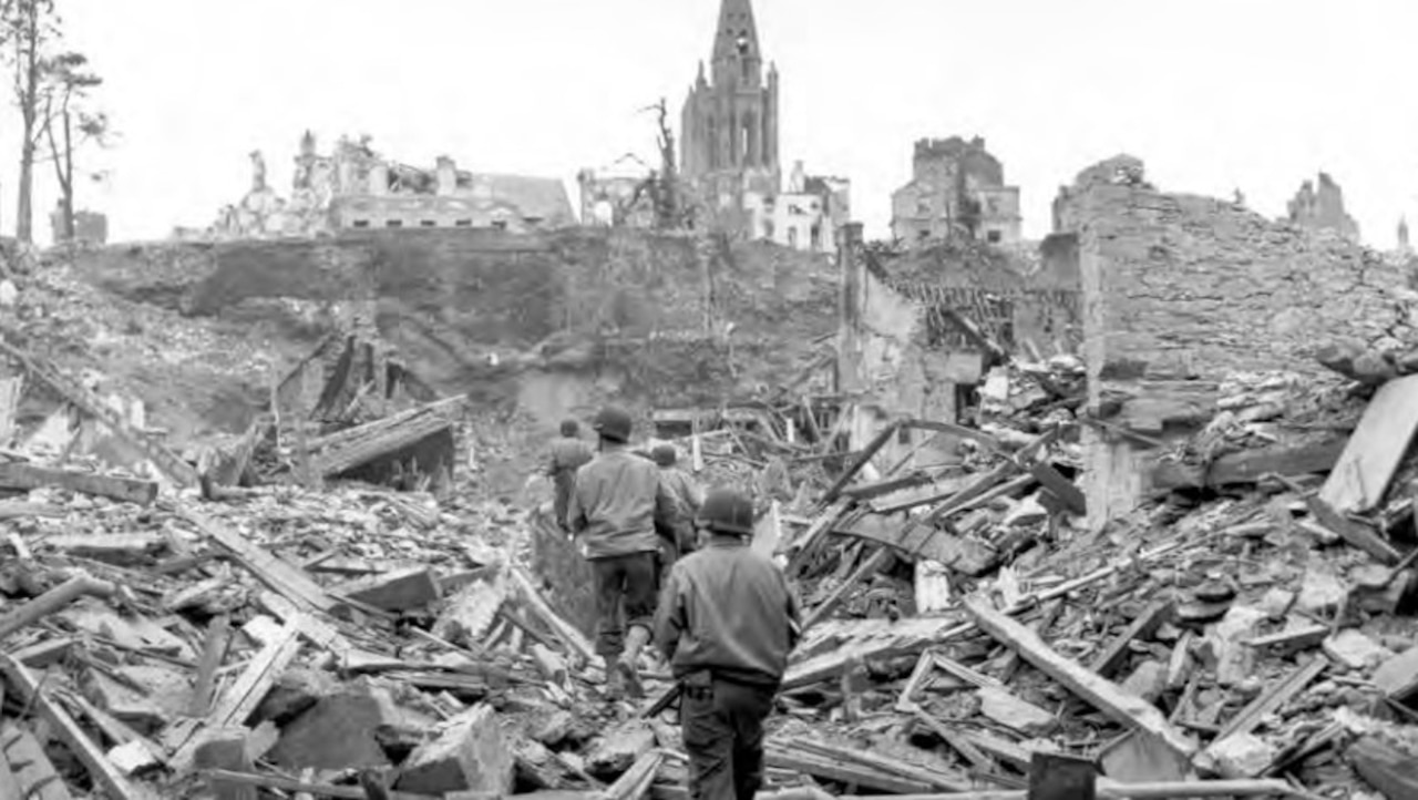 Soldiers walk through building debris in a destroyed town.