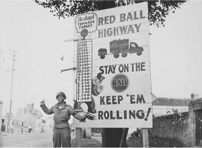 In this undated photo, a U.S. Army Soldier poses next to a sign indicating the Red Ball Express route. The 82-day operation was a critical logistics effort during WW II to supply the First and Third Armies as they advanced across France.  At its peak, the Red Ball Express delivered 12,500 tons of supplies per day.