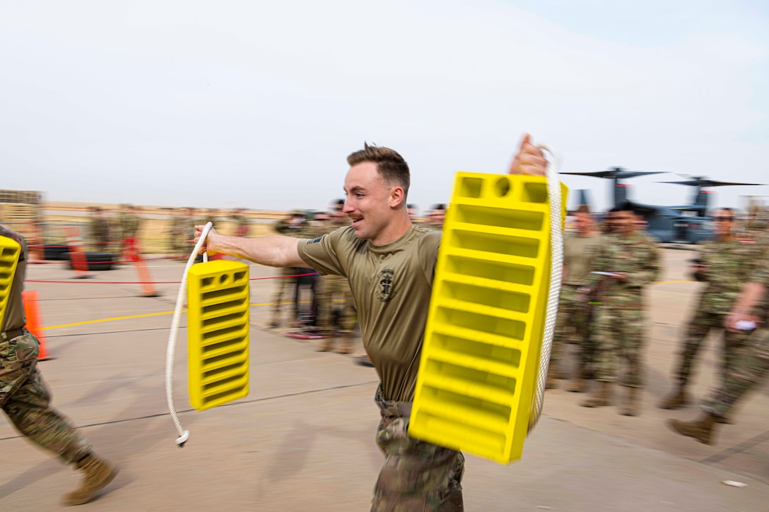 An airman carries wheel chocks as others stand around.