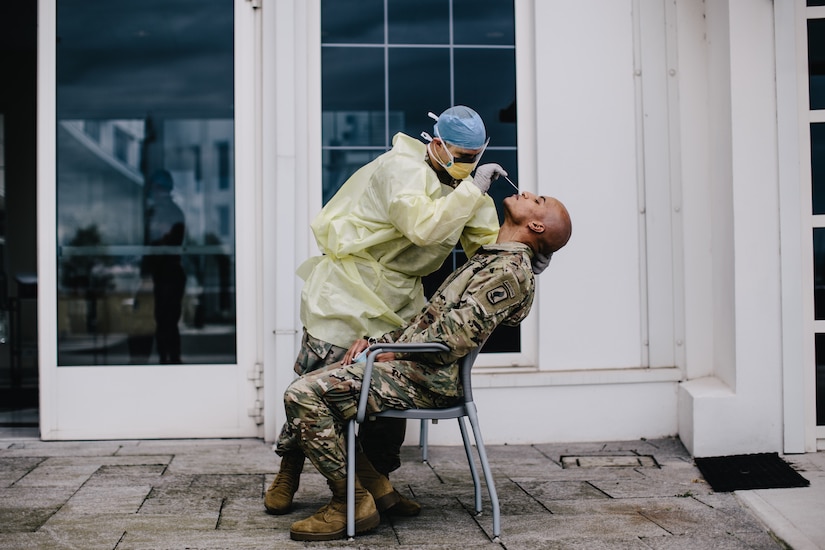 Army Medic in a medical gown administers a COVID test to a service member sitting in a chair in Italy.