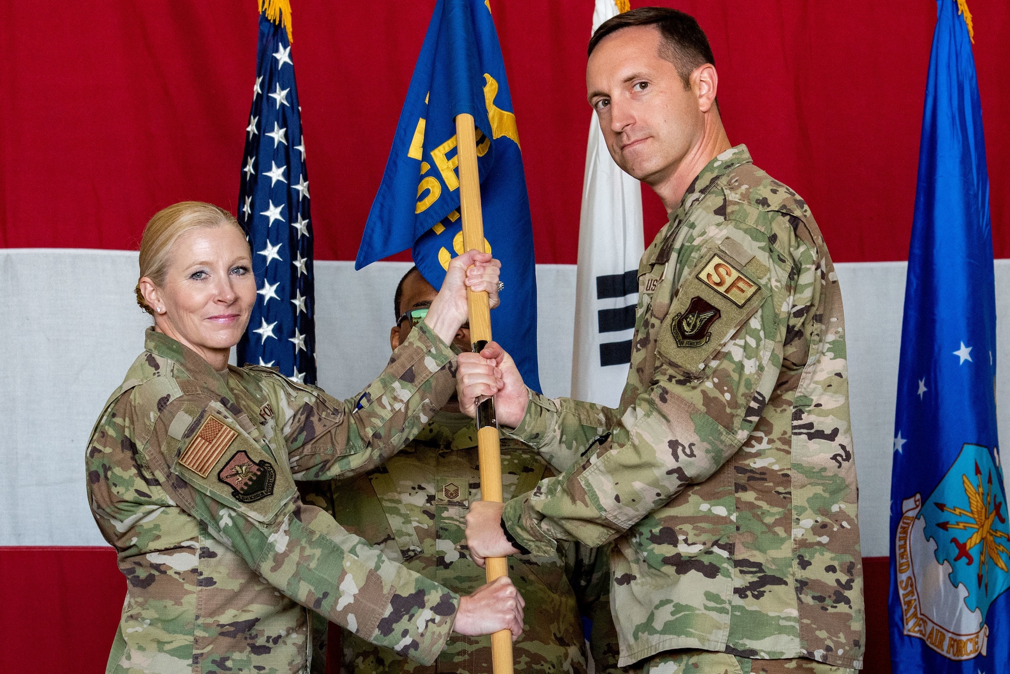 Col. Jonelle Eychner, 51st Mission Support Group commander, left, passes the squadron guidon to Lt. Col. Nicholas Brence, 51st Security Forces Squadron newly-appointed commander, as a symbol of his taking command of the SFS