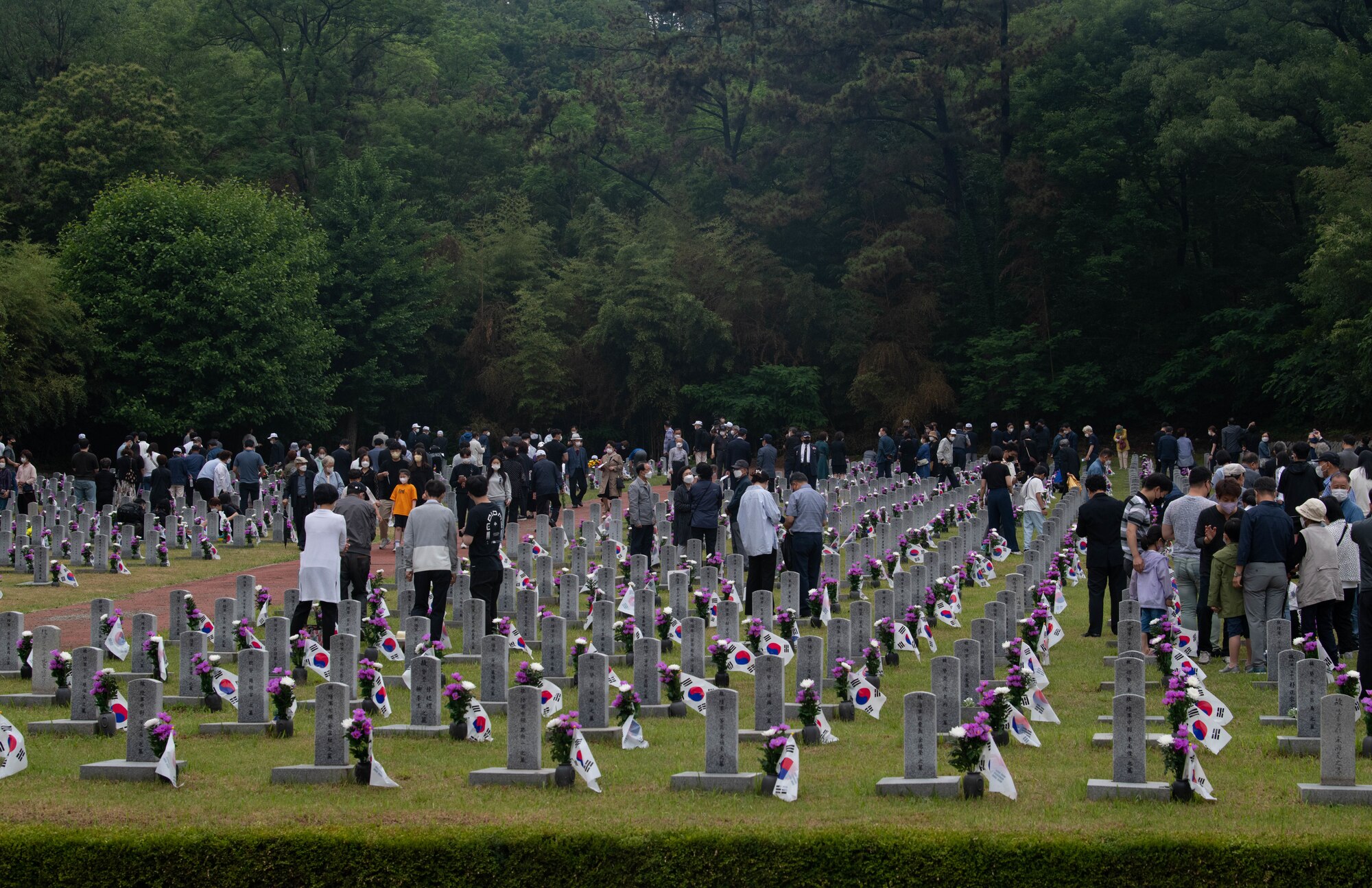 A graveyard with people placing flowers on graves.