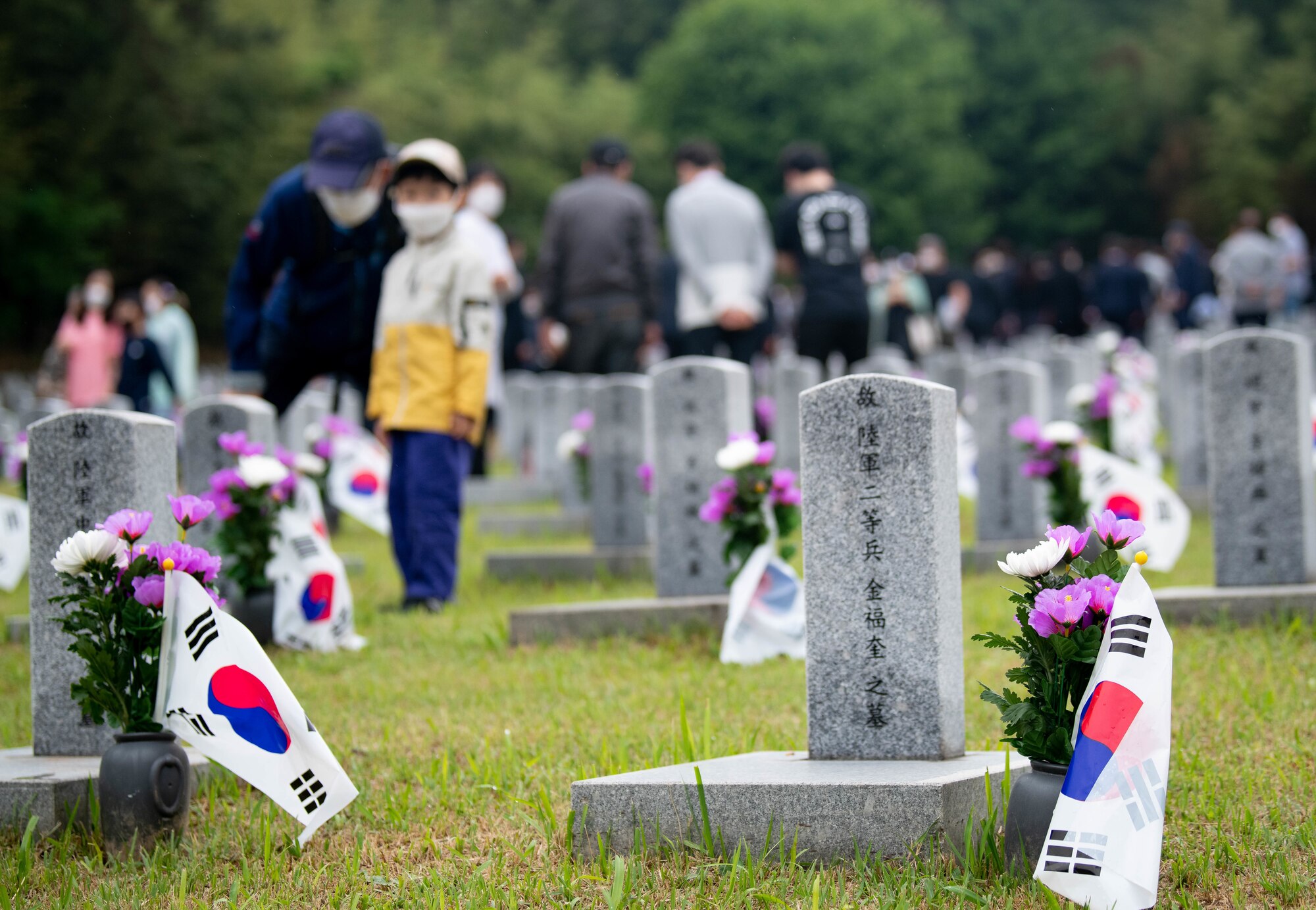 Tombstones in a graveyard with people placing flowers behind them.