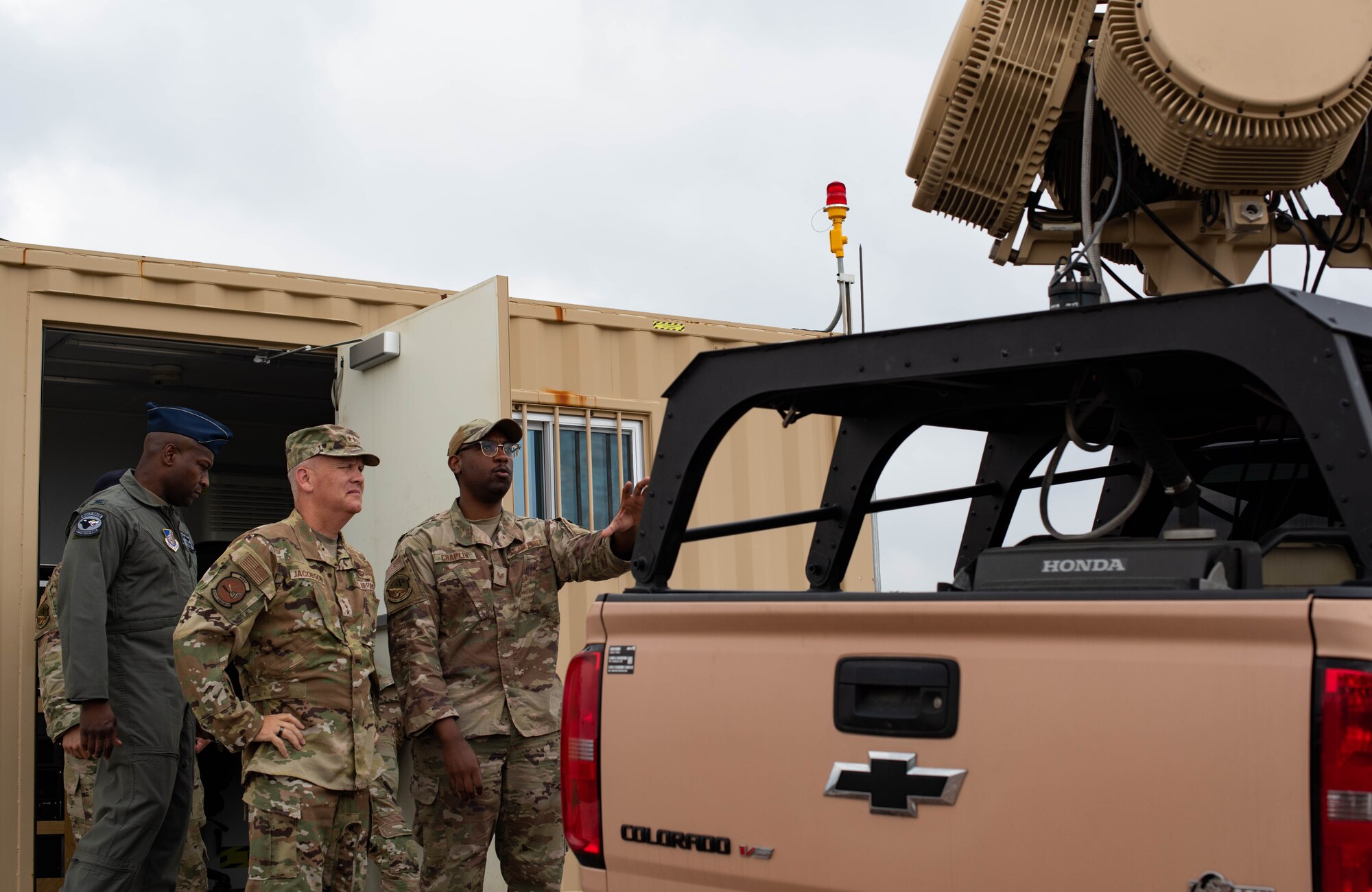 Three military members talk outside a pick-up truck.