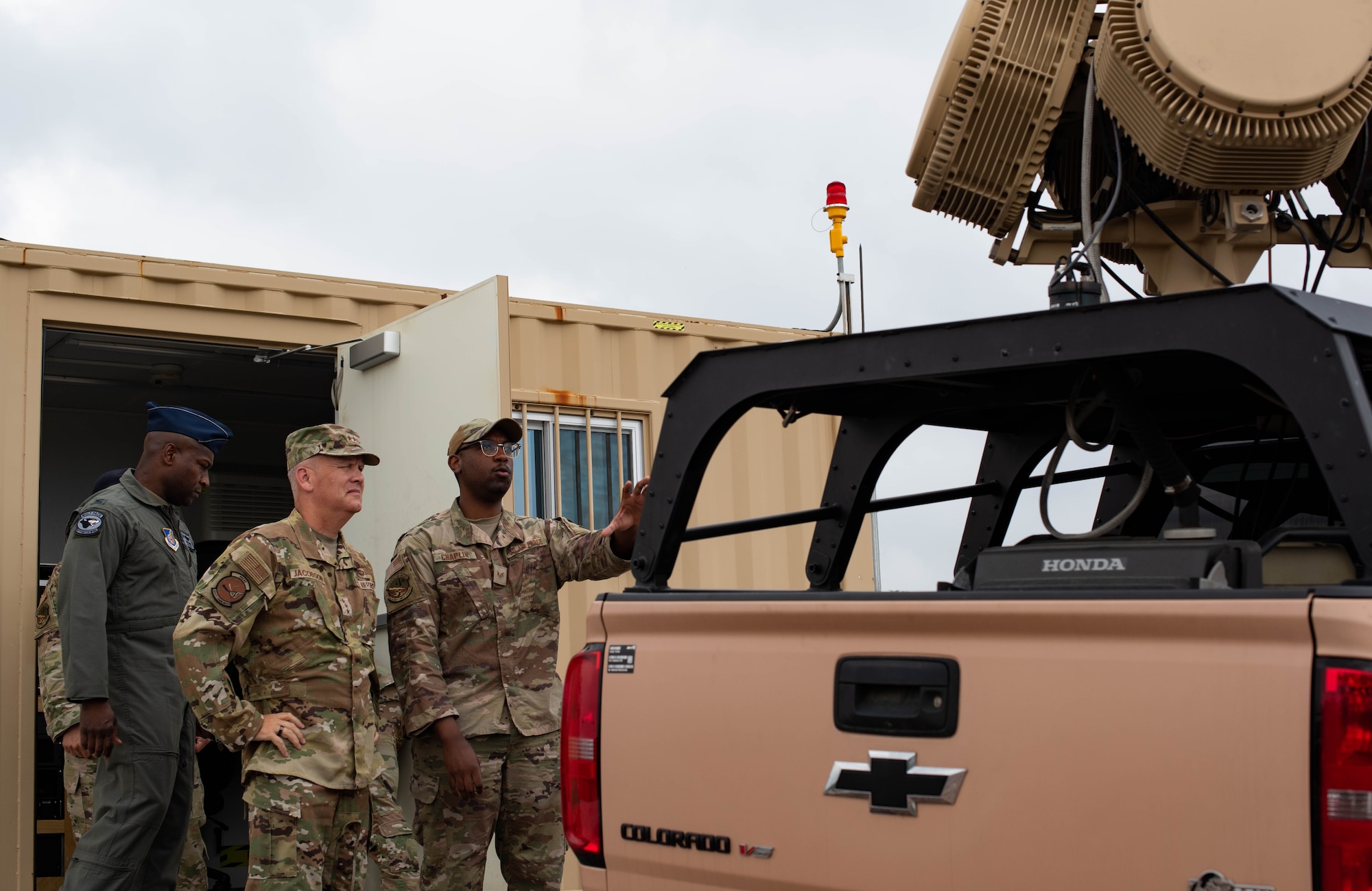 Three military members talk outside a pick-up truck.