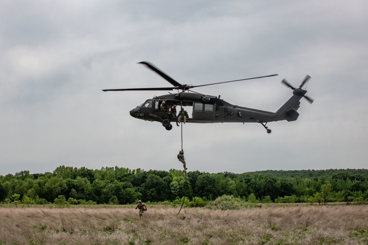helicopter hovers while military members slide down rope