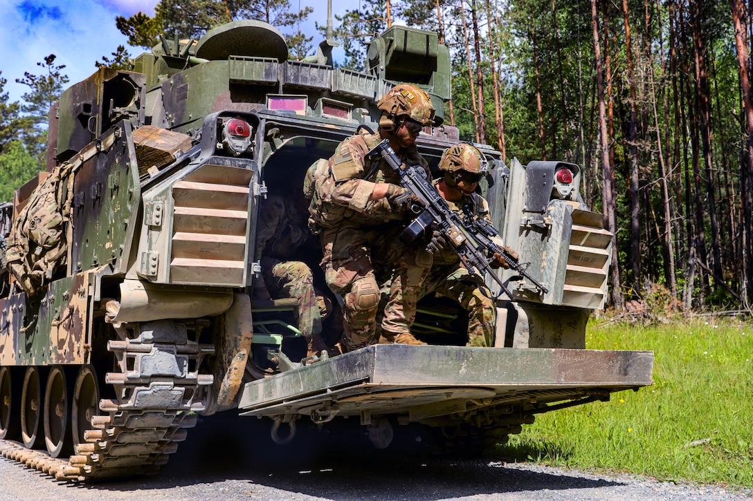 Soldiers holding weapons jump out of the back of a tank.