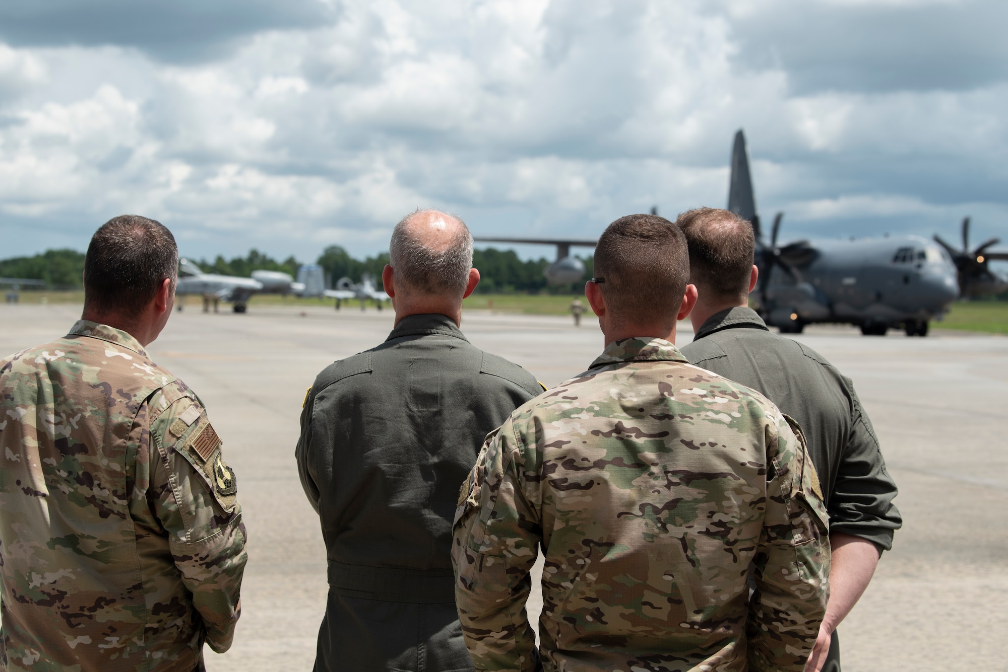 A photo of four Airmen standing together, with two A-10C Thunderbolt II's and an HC-130J Combat King II in the back ground.