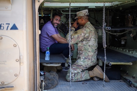 A Soldier and civilian sit inside of a military vehicle.