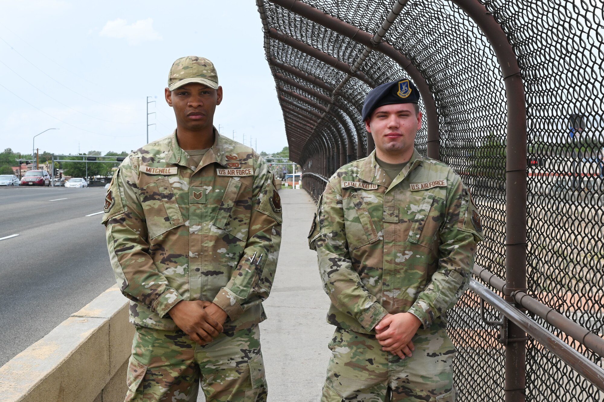 Two men stand together on an overpass.