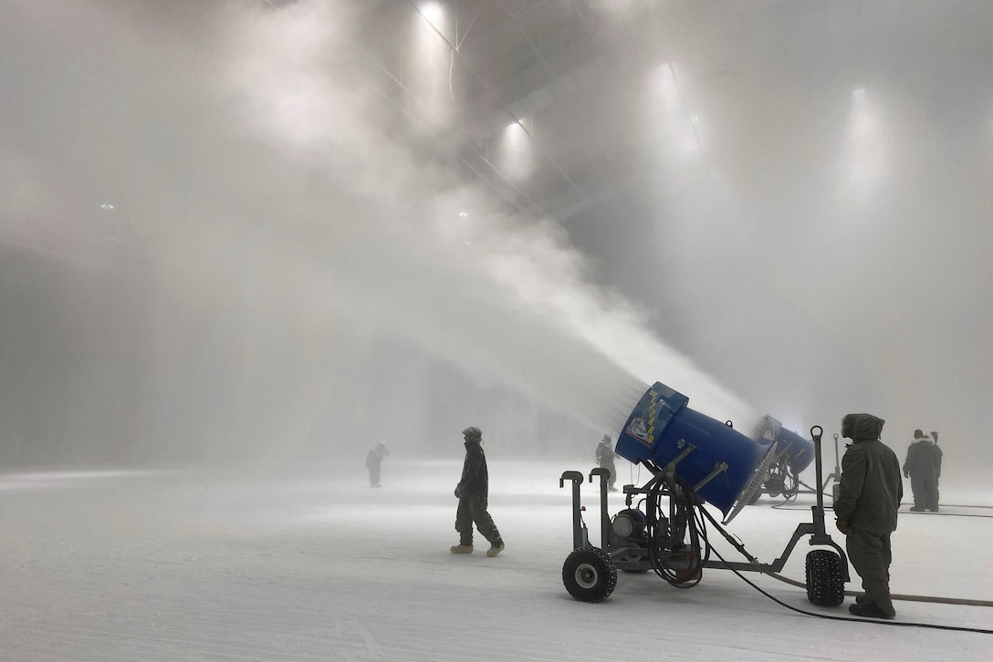 Service members use machines to create snow inside of a building.