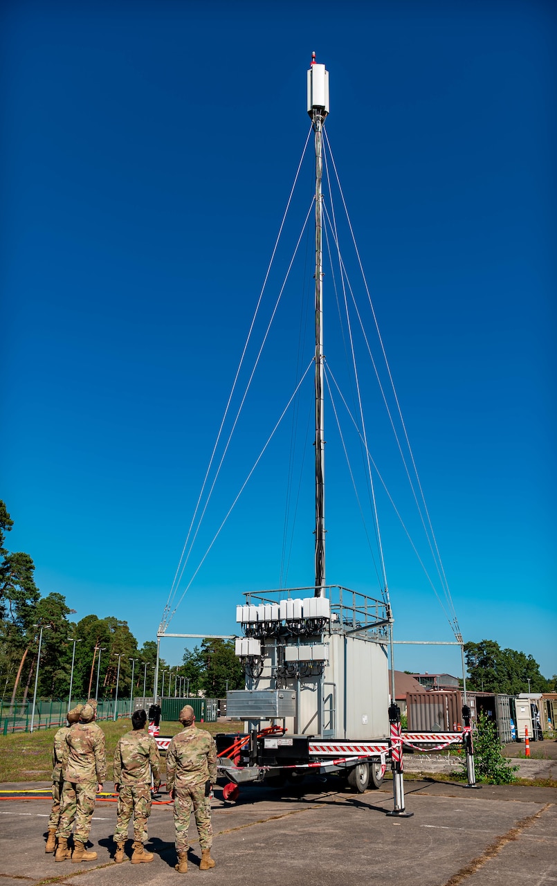 Service members look upward at an antenna.