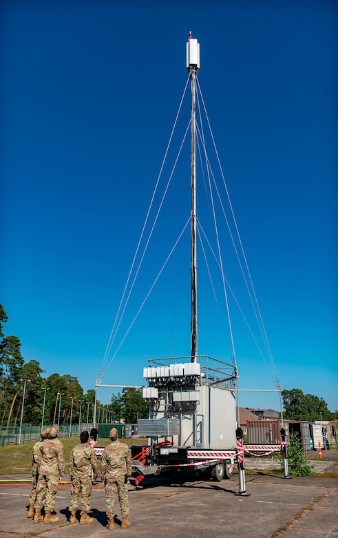 Service members look upward at an antenna.