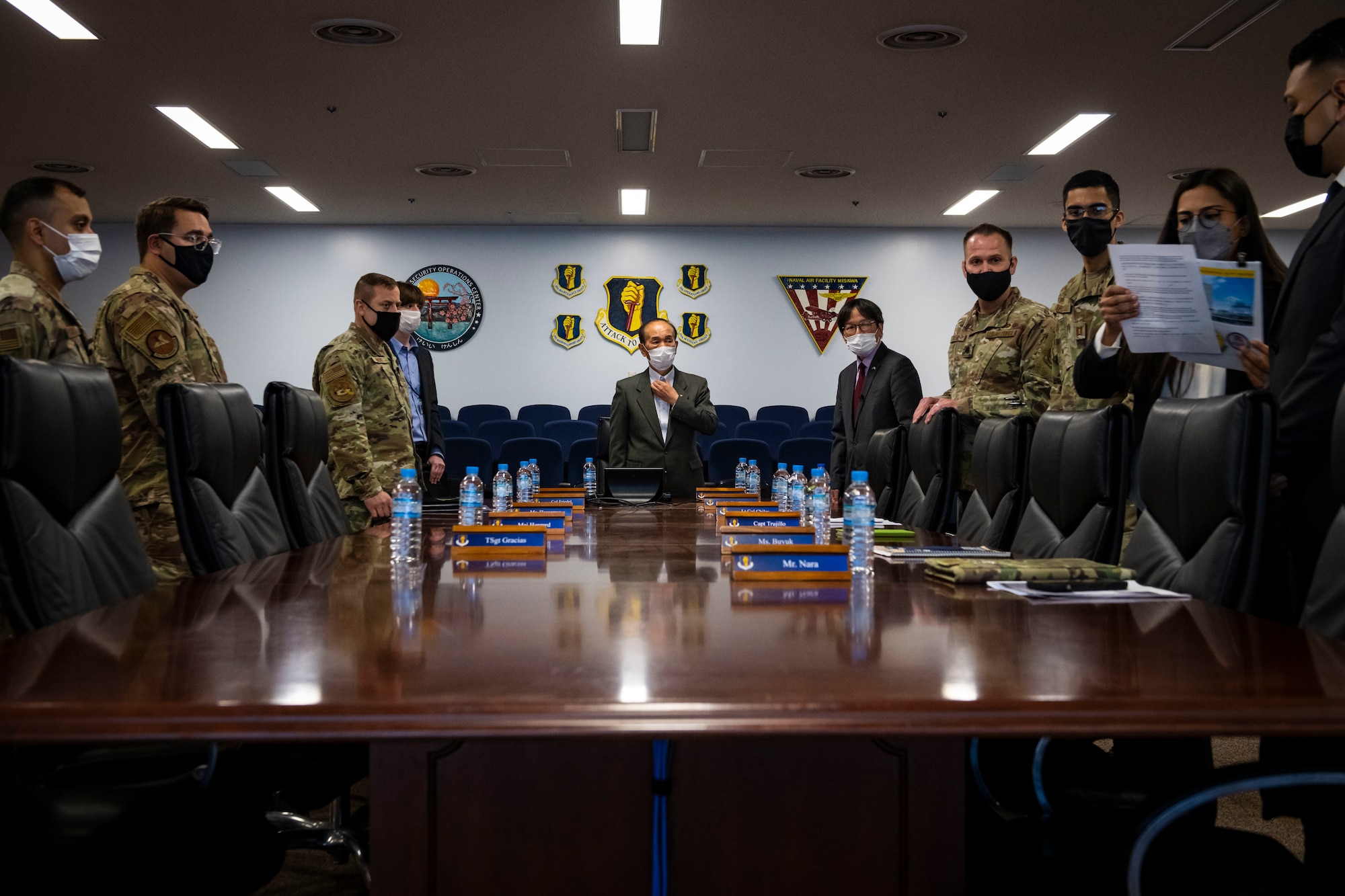 Military members and members in suits stand around a conference desk.