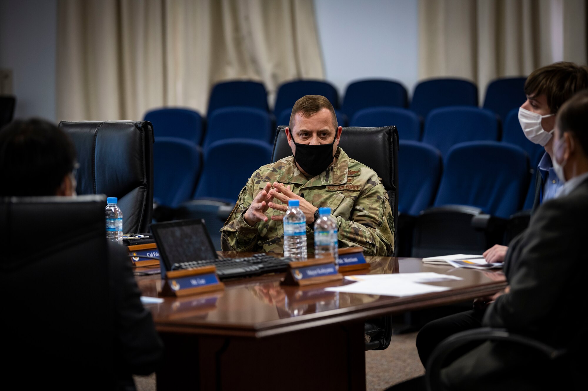 Military member talks to members in suits while sitting at a conference desk.