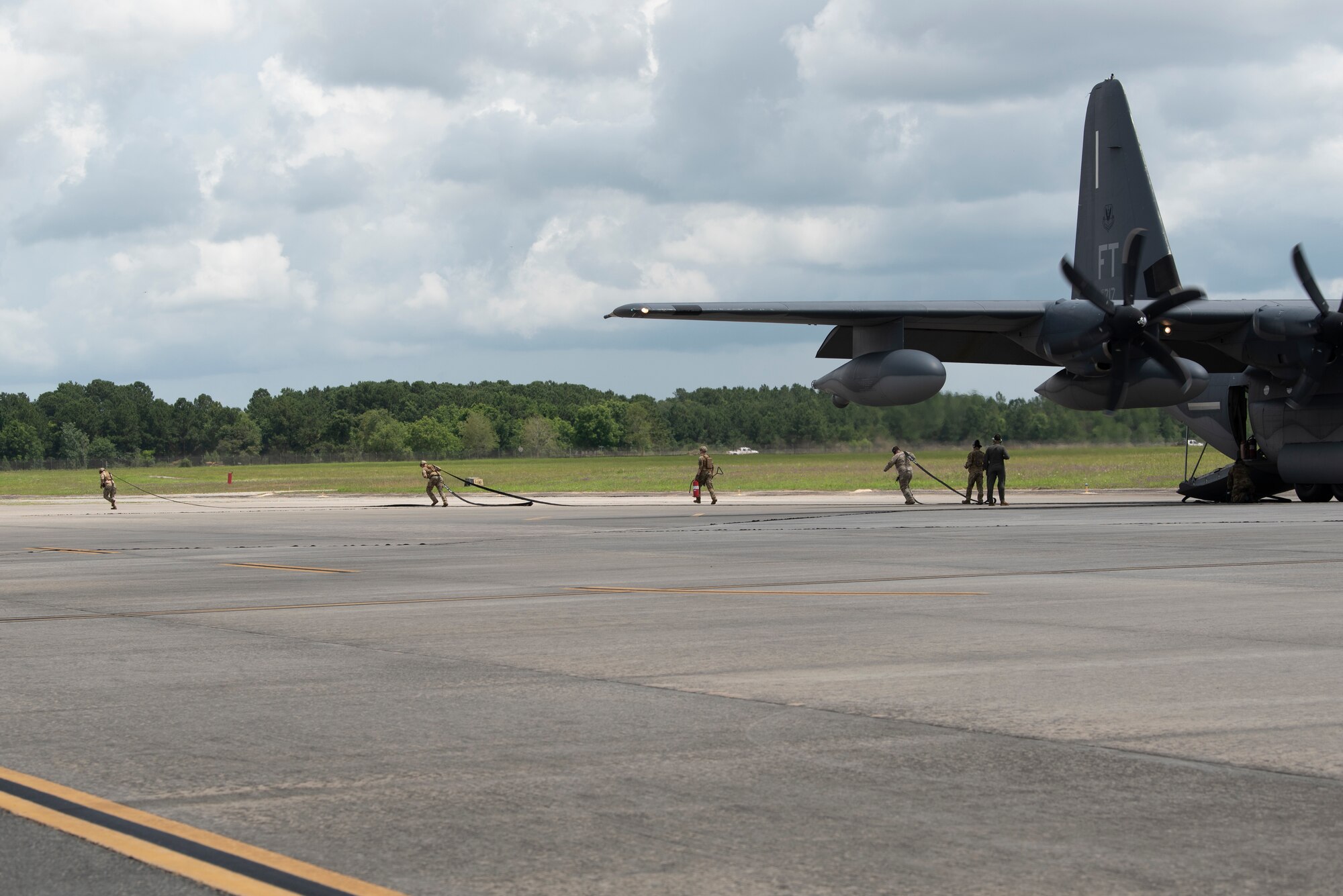 A photo of four Airmen running out of the back of an HC-130J Combat King II while carrying a fuel hose.