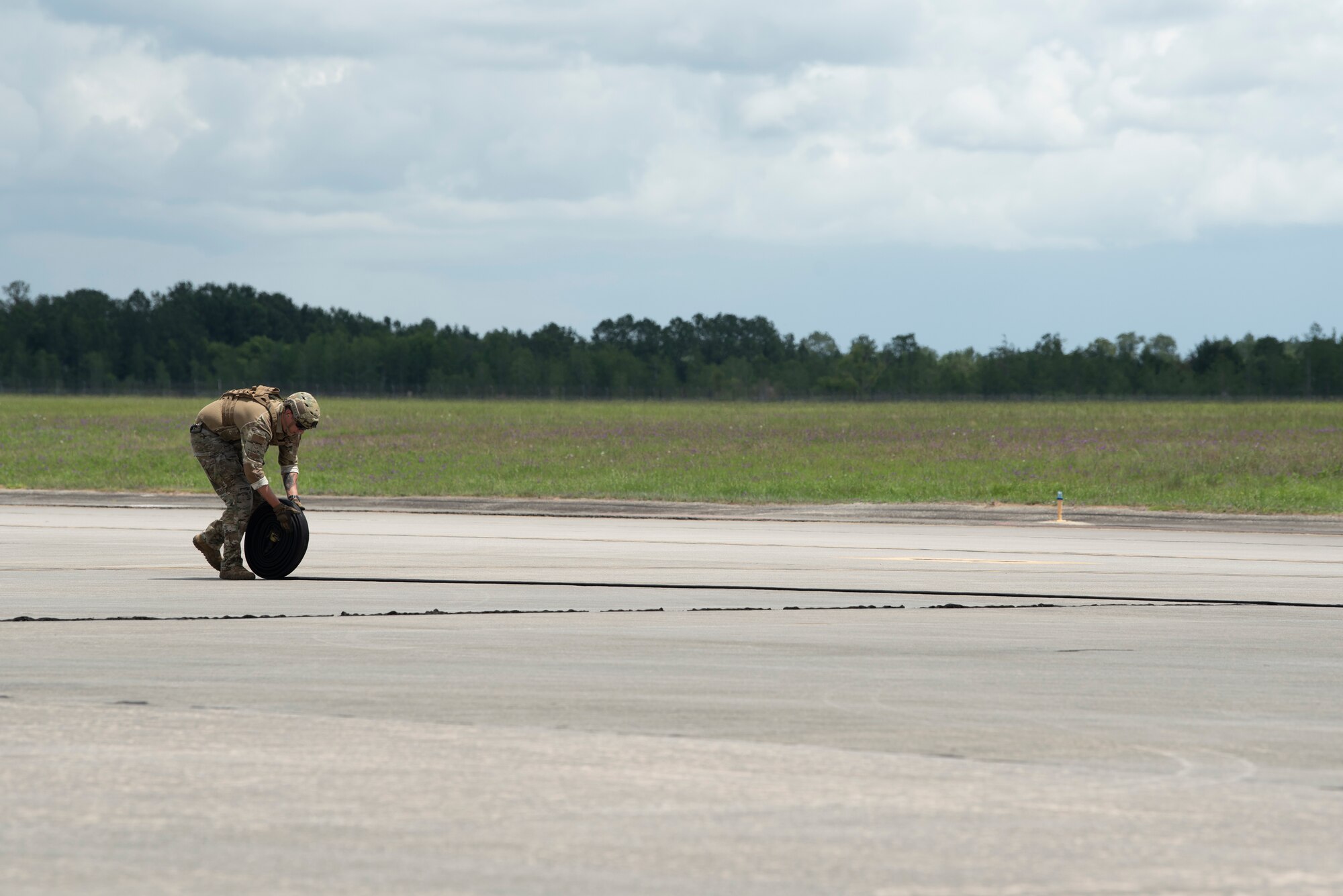 A photo of an Airmen rolling up a hose from the left side of the screen to the right.