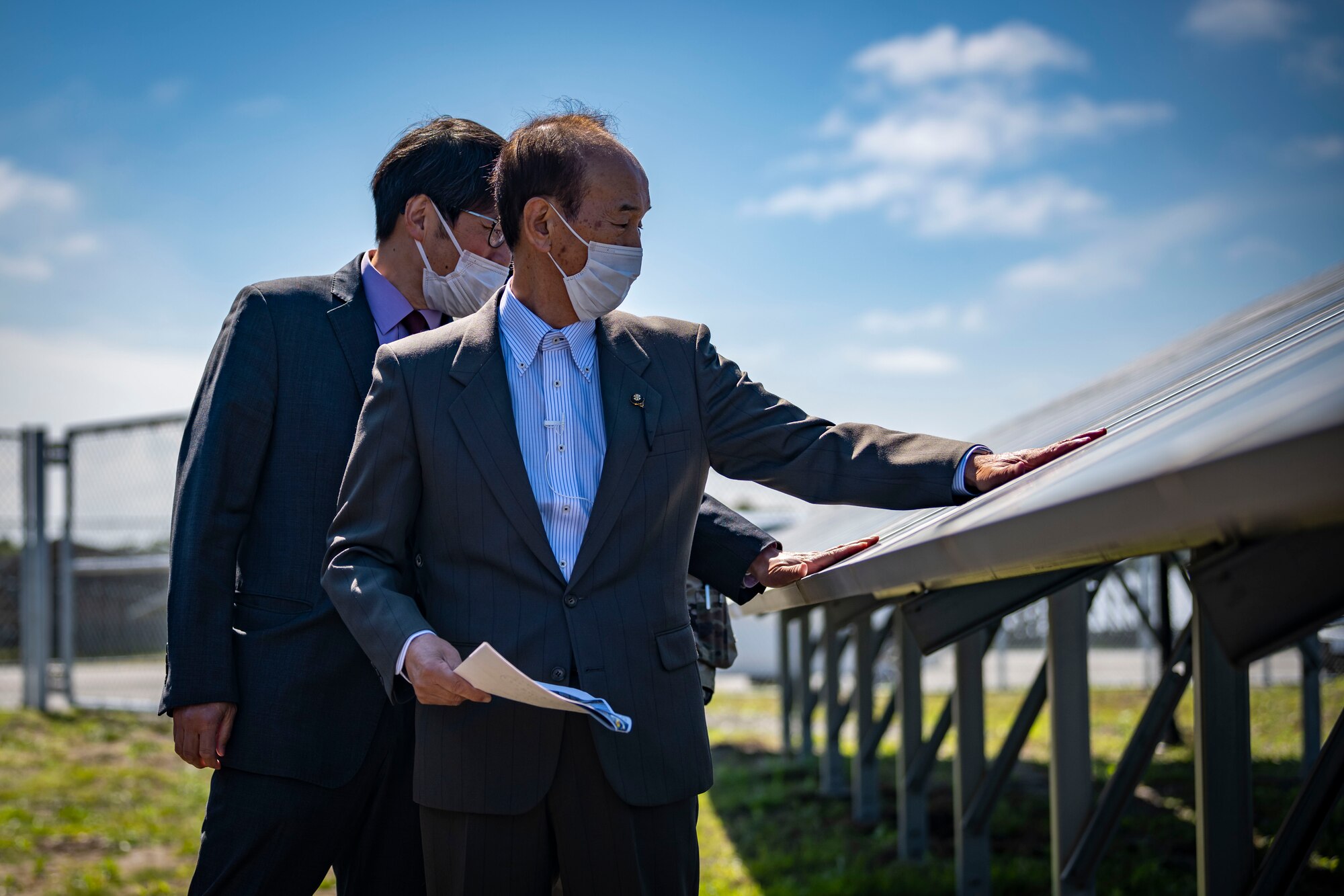 Members in suits place their hands on a solar panel.