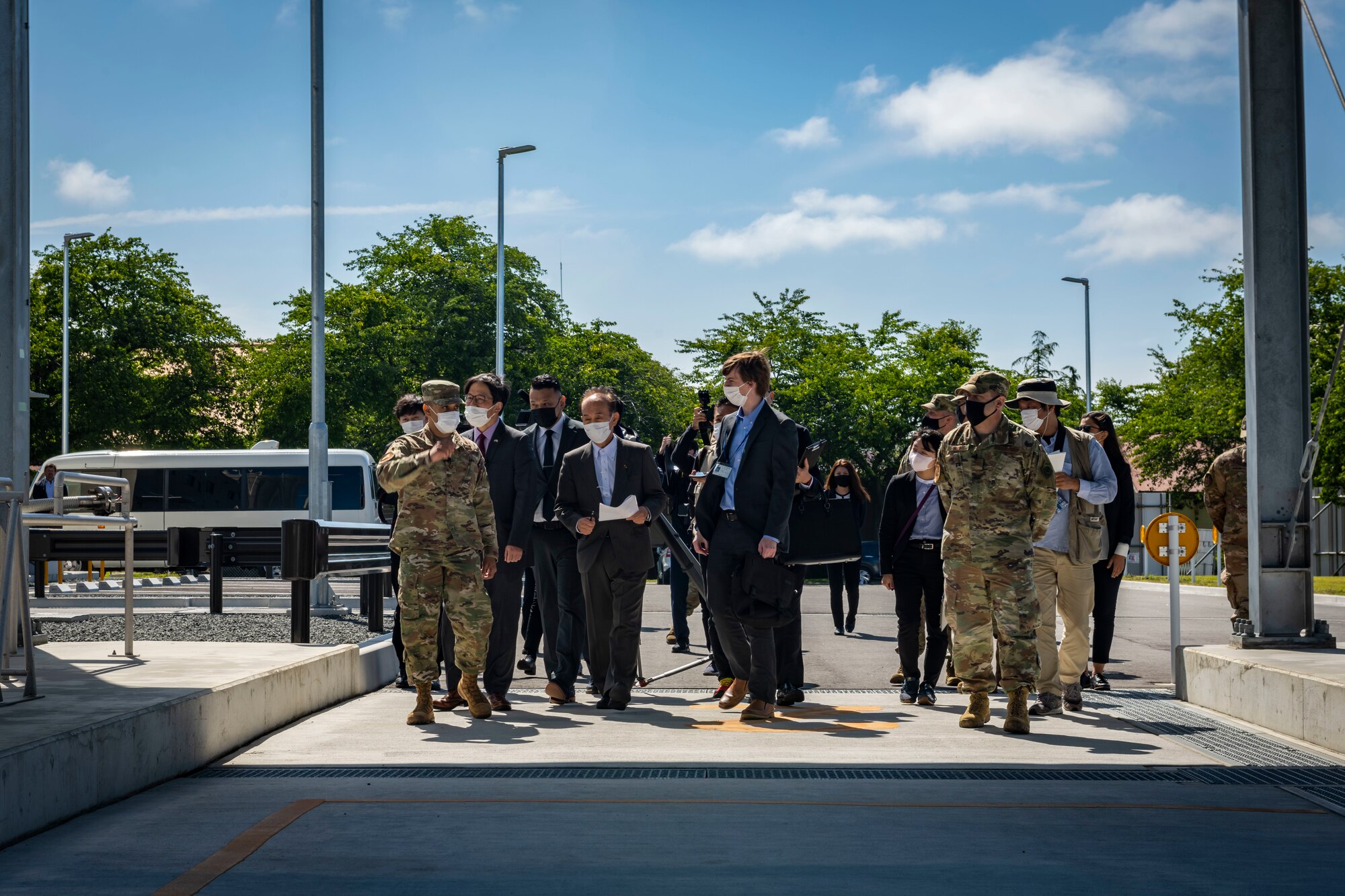 Military members in uniform and members in suits walk through a gas plant.