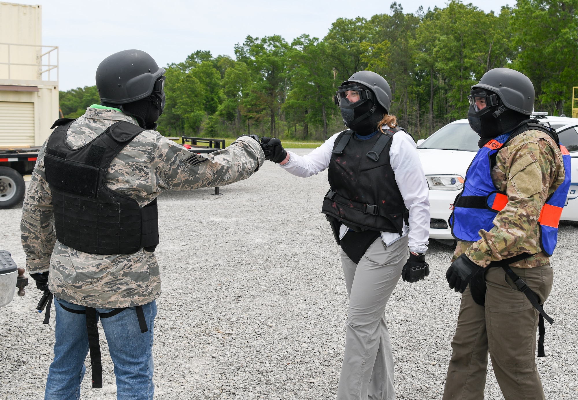 Man and woman in protective gear for using Simunitions weapons fist bump as another man watches