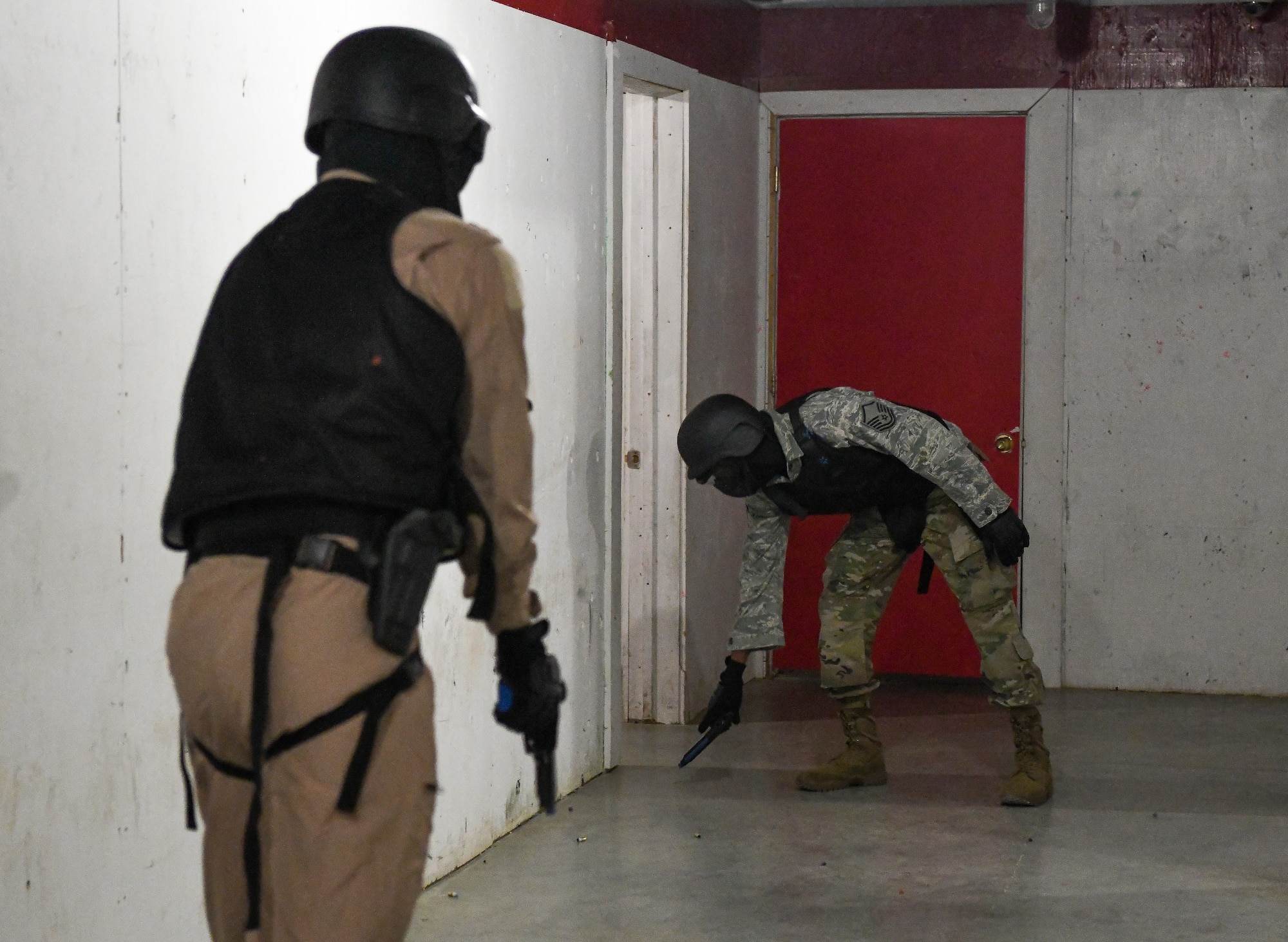 Two men with Simunitions weapons in hallway with one setting weapon on ground