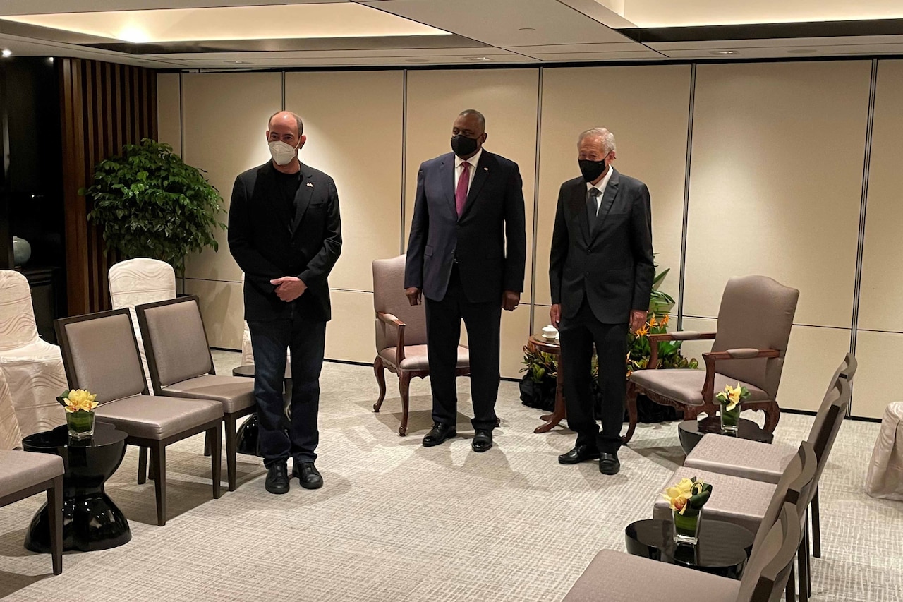 Three men wearing suits and face masks stand side-by-side and pose for a photo.