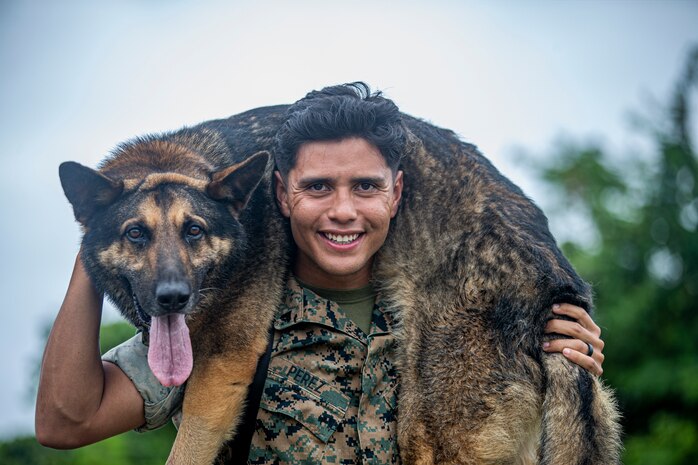 U.S. Marine Corps Cpl. Ivan Perez, a military working dog handler, and his partner, Jack, a military working dog with Provost Marshal's Office, Marine Corps Base Camp Smedley D. Butler, pose for a photo on Camp Hansen, Okinawa, Japan, May 26, 2022. Perez and Jack, an 80-pound German Shepherd, specializing in explosives detection, have trained together for nearly a year. PMO K-9 teams are on continuous shifts on all bases in Okinawa, trained and prepared for emergencies such as suspect apprehension, pursuit attacks, building searches, field scouting, drug and explosives detection.