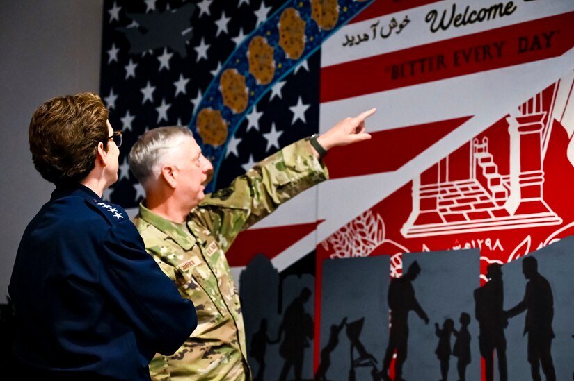 U.S. Air Force Gen. Jacqueline Van Ovost, U.S. Transportation Command commander, and U.S. Air Force Maj. Gen. Mark Camerer, U.S. Air Force Expeditionary Center commander, view a mural in memory of Operation Allies Welcome at Joint Base McGuire-Dix-Lakehurst, New Jersey, June 3, 2022. Van Ovost toured the center, coined Airmen for their services during OAW, and addressed recent graduates of the Advanced Study of Air Mobility course.