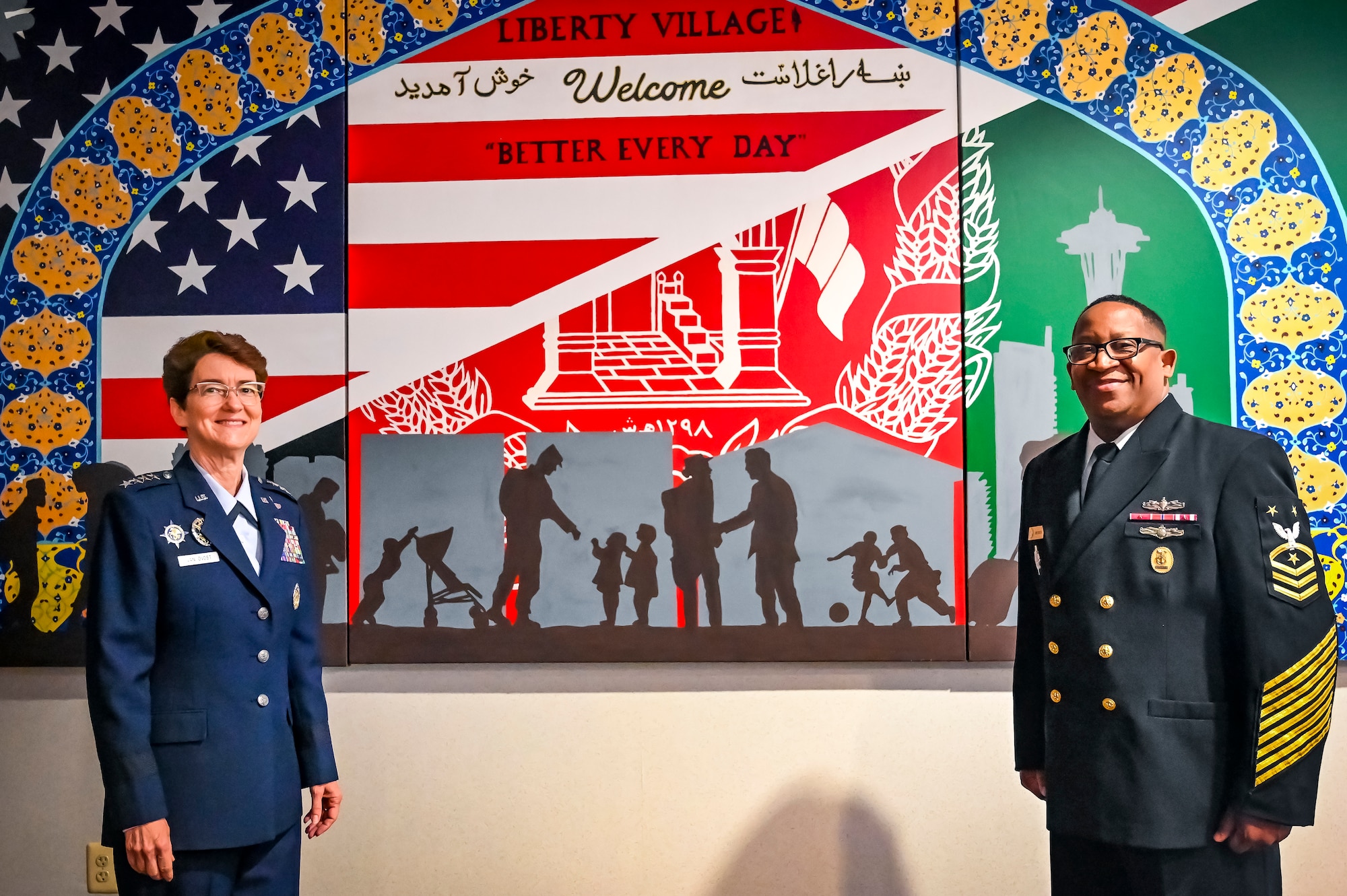 U.S. Air Force Gen. Jacqueline Van Ovost, U.S. Transportation Command commander, and U.S. Navy Fleet Master Chief Petty Officer Donald O. Myrick, U.S. Transportation Command senior enlisted leader, pose in front of a mural in memory of Operation Allies Welcome at Joint Base McGuire-Dix-Lakehurst, New Jersey, Jun. 3, 2022. Van Ovost toured the center, coined Airmen for their services during OAW, and addressed recent graduates of the Advanced Study of Air Mobility course.