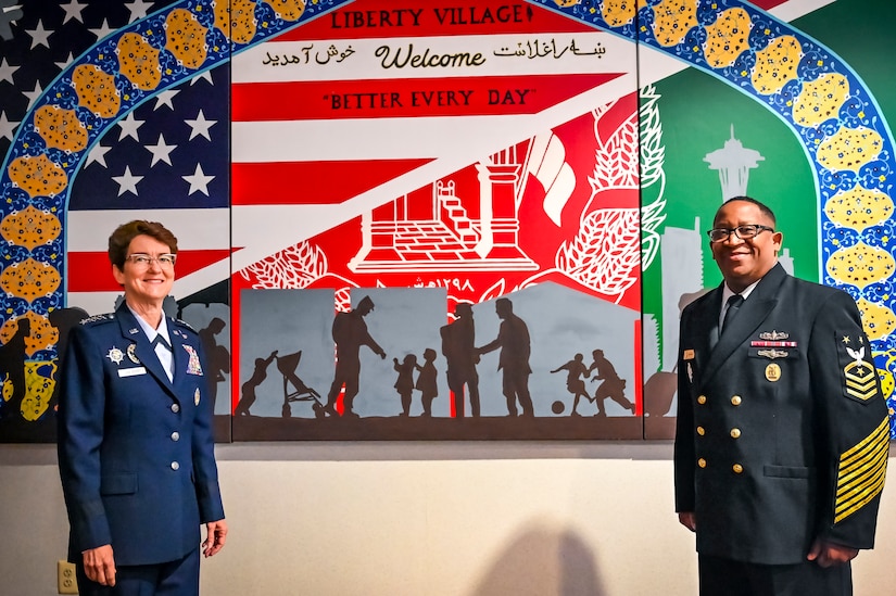 U.S. Air Force Gen. Jacqueline Van Ovost, U.S. Transportation Command commander, and U.S. Navy Fleet Master Chief Petty Officer Donald O. Myrick, U.S. Transportation Command senior enlisted leader, pose in front of a mural in memory of Operation Allies Welcome at Joint Base McGuire-Dix-Lakehurst, New Jersey, Jun. 3, 2022. Van Ovost toured the center, coined Airmen for their services during OAW, and addressed recent graduates of the Advanced Study of Air Mobility course.